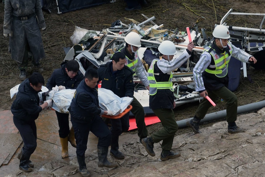 Military police lead workers carrying a victim's body at the crash site of the TransAsia plane