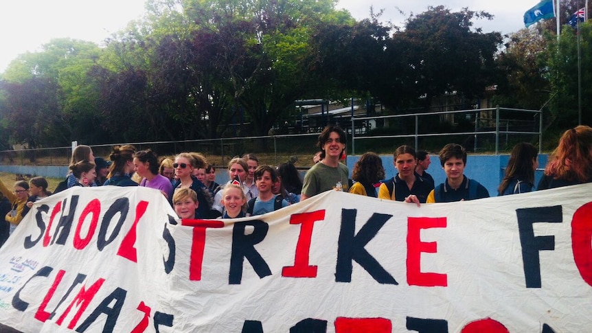 School children holding a large banner reading 'School Strike for Climate Change' in red and black letters