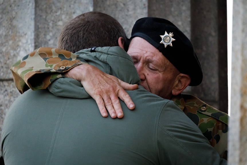 A man wearing a military beret hugs another man.