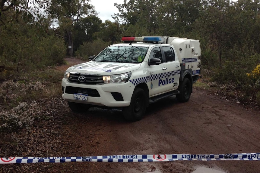 A police car parked in bushland behind a cordoned off area.