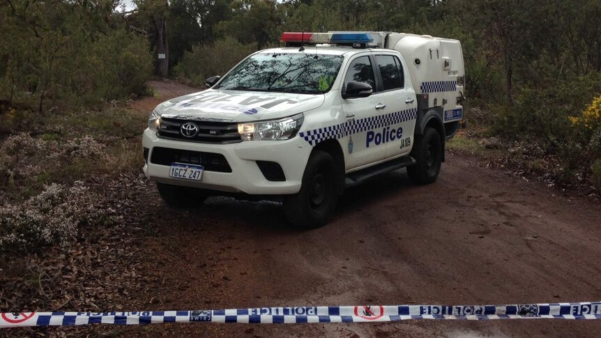 A police car parked in bushland behind a cordoned off area.