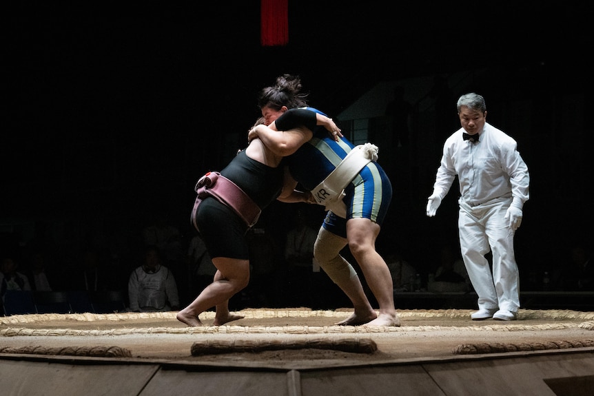 Two women with their arms wrapped around each other in a sumo ring 