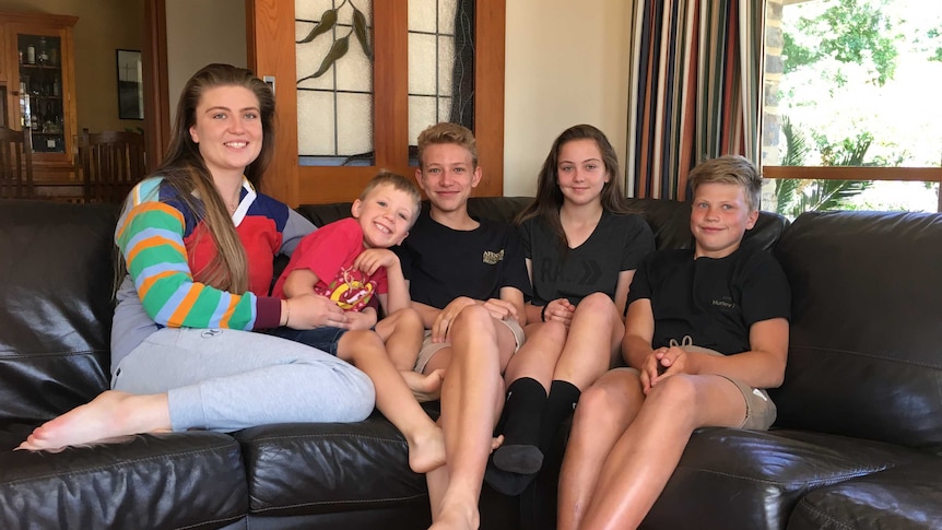 Five children of varying ages sit on a couch in a living room.