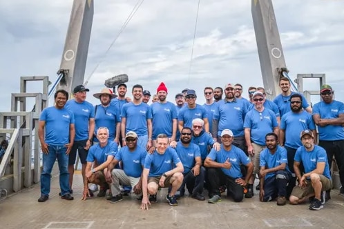 A group of people wearing blue shirts pose for a photo on the deck of a boat out at sea
