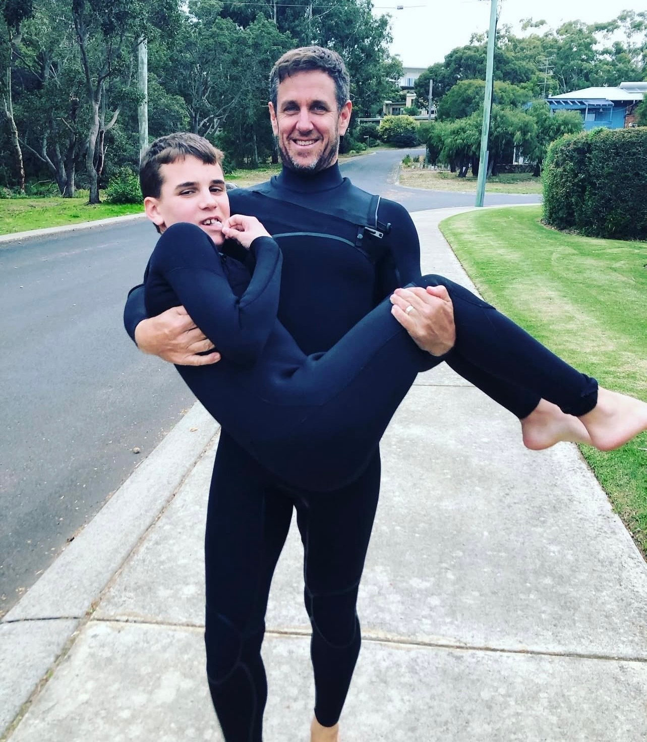 Un hombre carga a su hijo, ambos en trajes de neopreno.