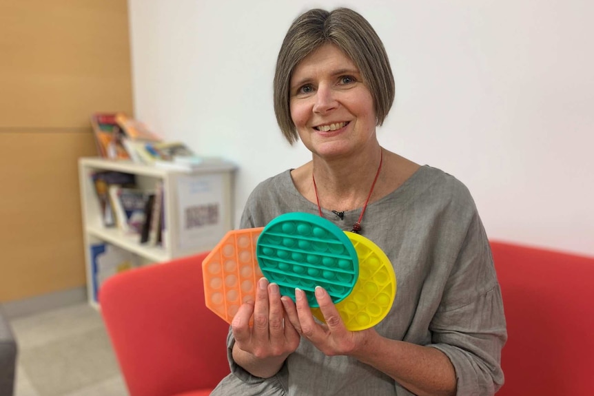 a woman hold up three multi-colour soft plastic toys and smiling