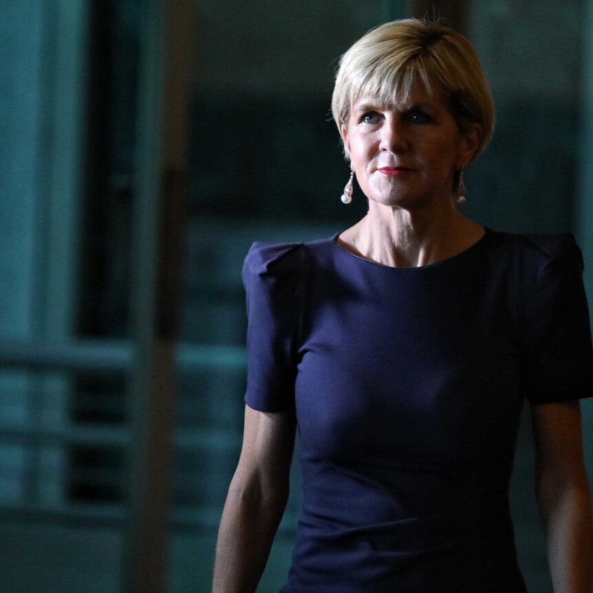 Foreign Minister Julie Bishop walks to a press conference. She's in shadow and wearing a blue dress.