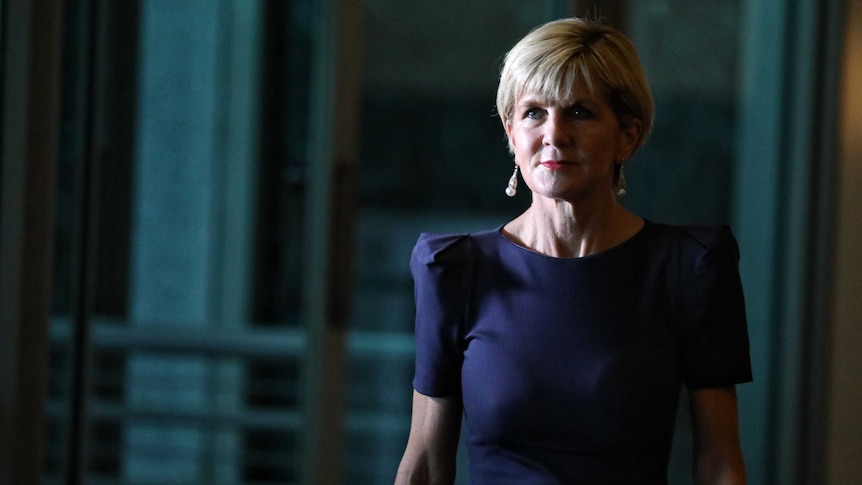 Foreign Minister Julie Bishop walks to a press conference. She's in shadow and wearing a blue dress.