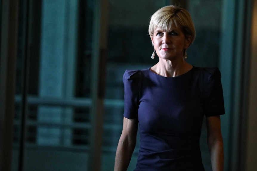 Foreign Minister Julie Bishop walks to a press conference. She's in shadow and wearing a blue dress.