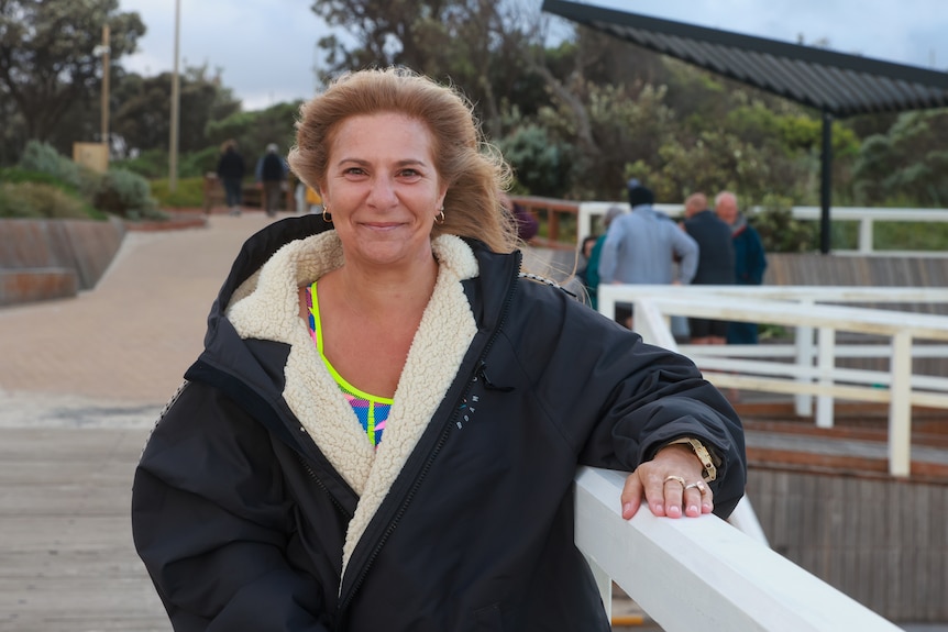 Nicole Chester leaning against a railing wearing a heavy jacket and grinning.