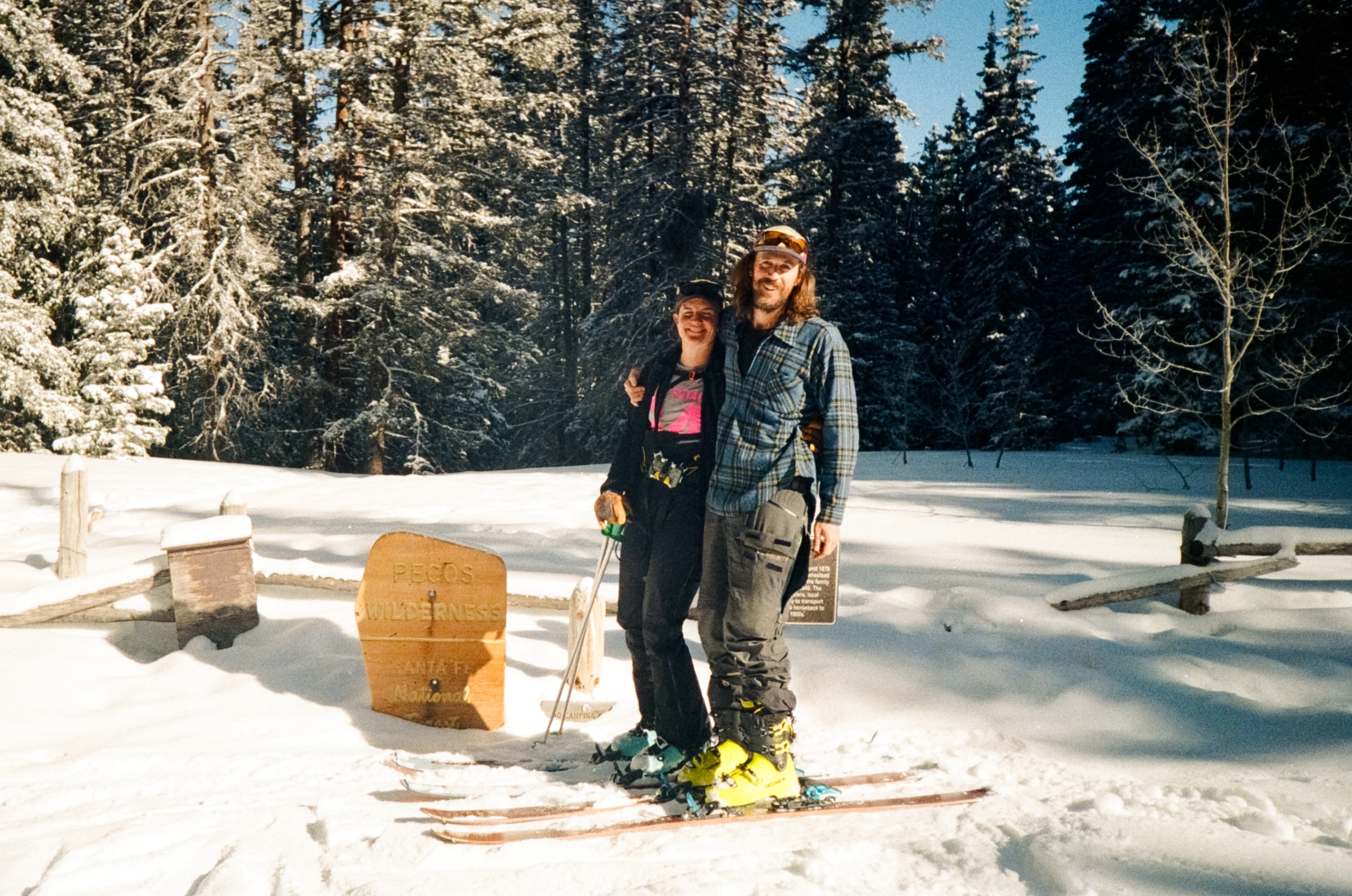A couple stands together with arms around each other while on skis in the snow.