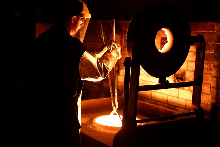 A man wearing protective clothing performing a gold pour. 