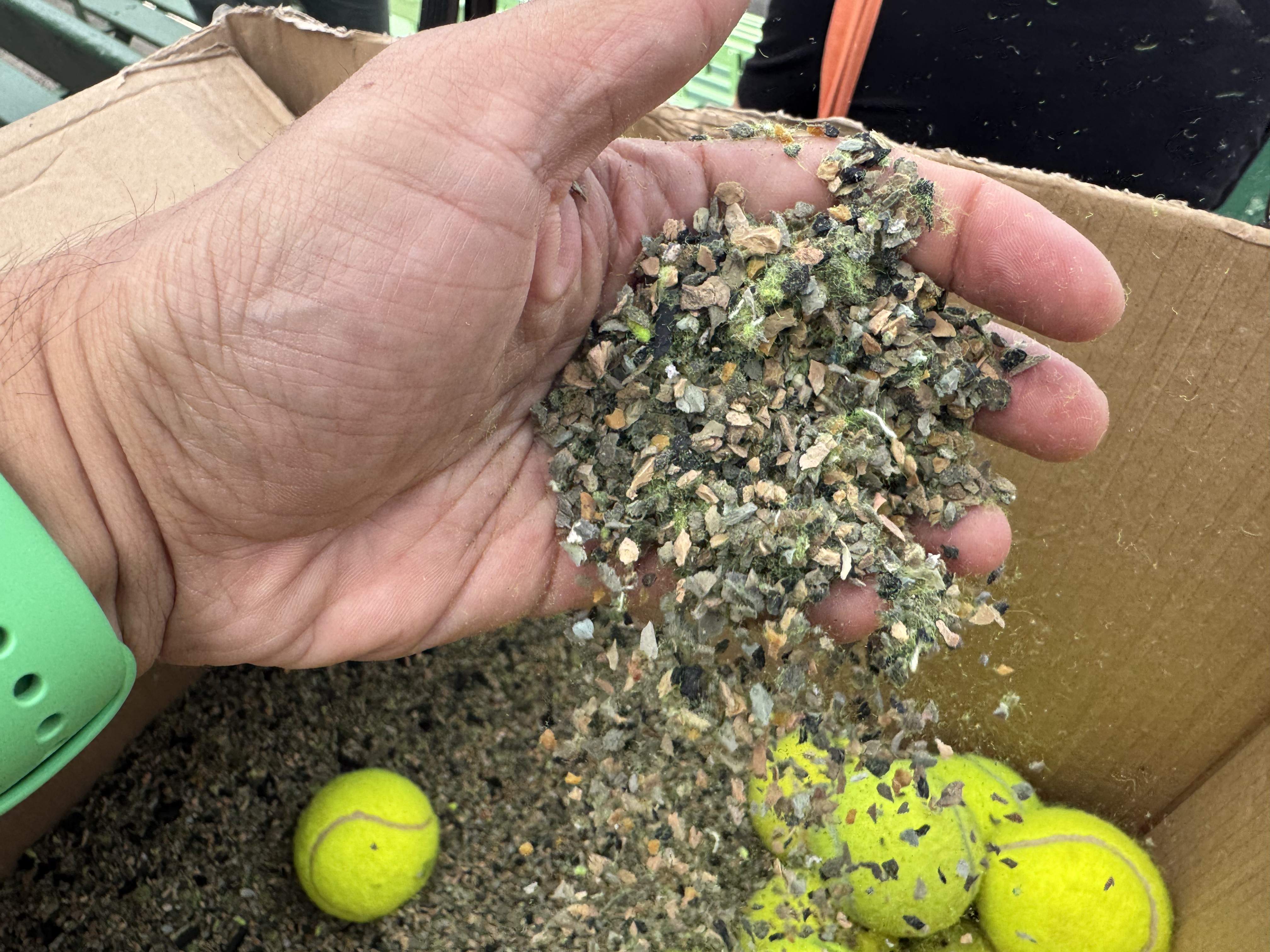 Una mano recoge un puñado de pelotas de tenis trituradas.