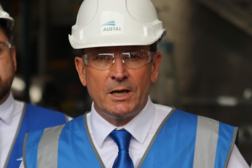 WA Premier Mark McGowan speaking at a media conference wearing a blue hi-vis vest, safety glasses and a white hard hat.