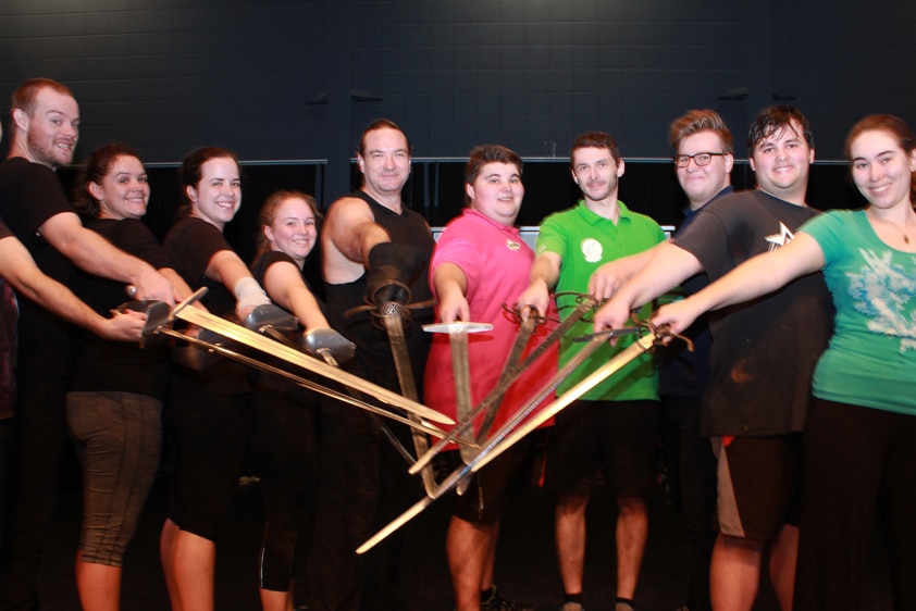 Group photo of students and teacher with swords pointing at the camera