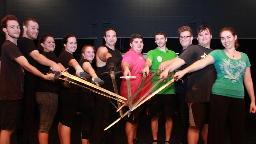 Group photo of students and teacher with swords pointing at the camera