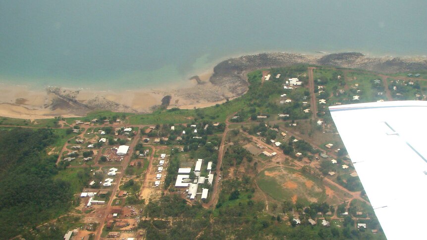 Aerial shot of the Galiwinku community, shows a scattering of buildings in a lush, green area near a shoreline.