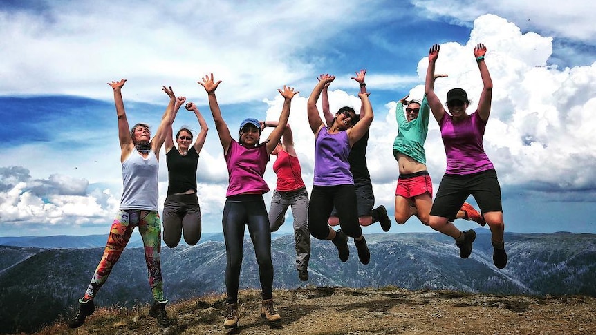 Eight women jump for joy on top of a mountain.