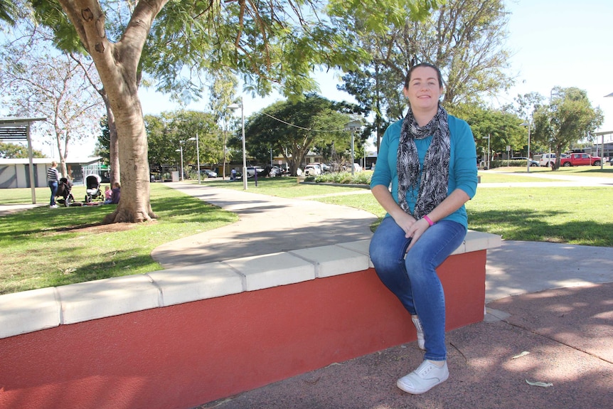 A woman sits on a ledge in a park surrounded by trees