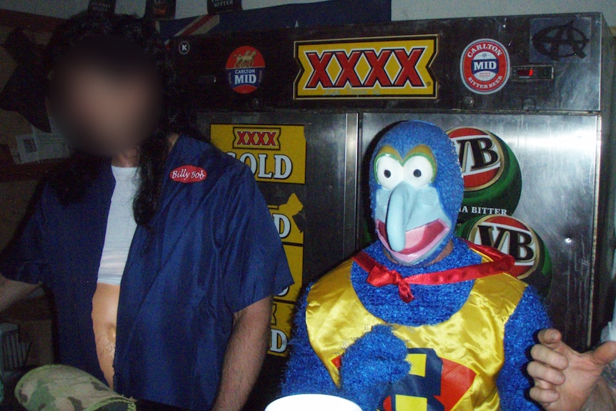Two people in costume behind a bar with XXXX Gold and VB beer signage. One wears a curly wig and the other is dressed as Gonzo.