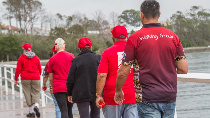 Walkers walk in a straight file along Moreton Bay.