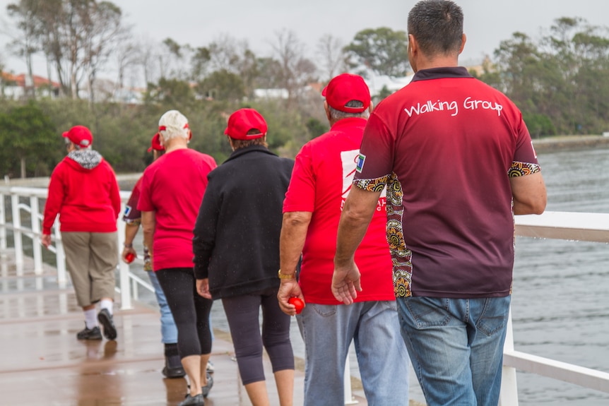 Walkers walk in a straight file along Moreton Bay.