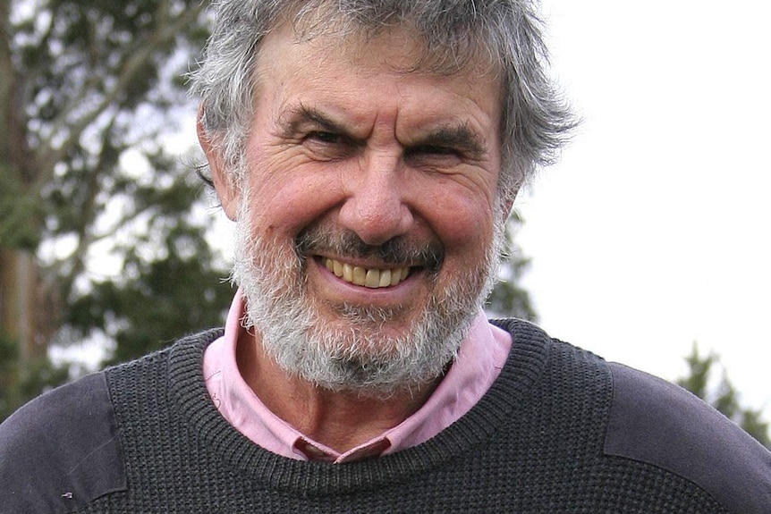 A bearded man smiles while standing outside.