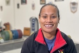 Woman seated in chair wearing navy blue jumper smiles at camera.