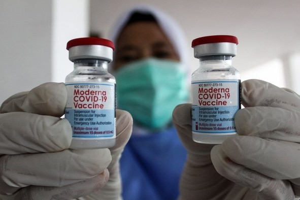 Two vials of the Moderna COVID vaccine are held up by a person wearing PPE.