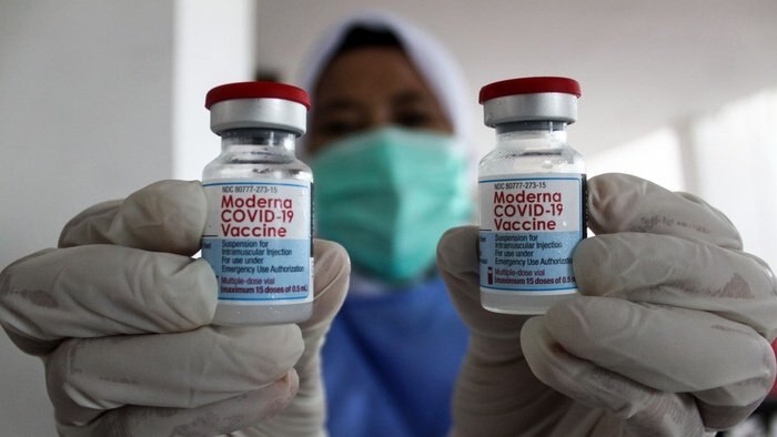 一个戴着面罩和手套的人拿着几瓶莫德纳疫苗。