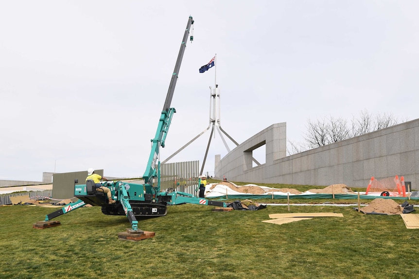 A crane installs a fence around the grassy hill of Parliament House.