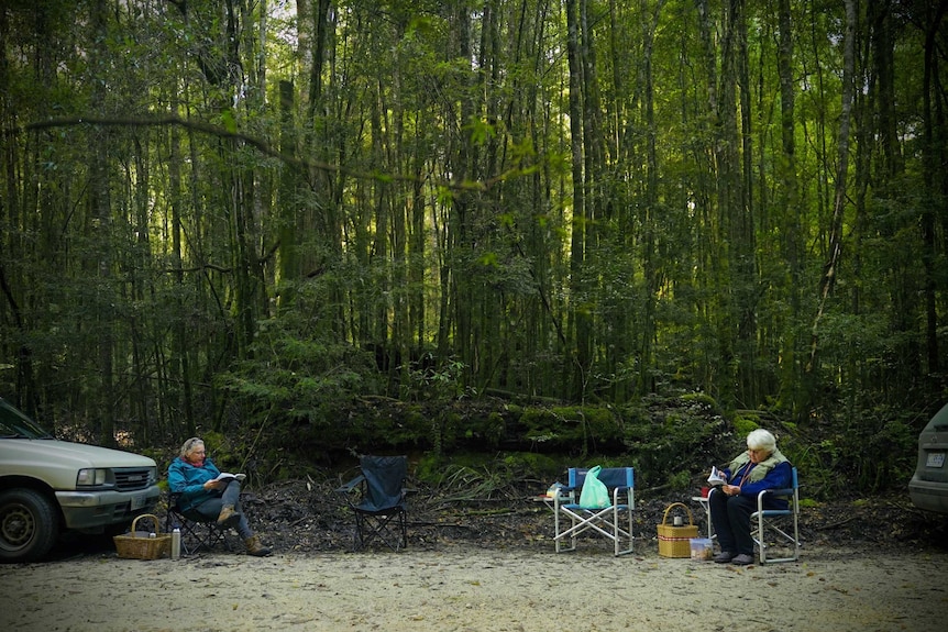 Two women sit reading by the side of a road.