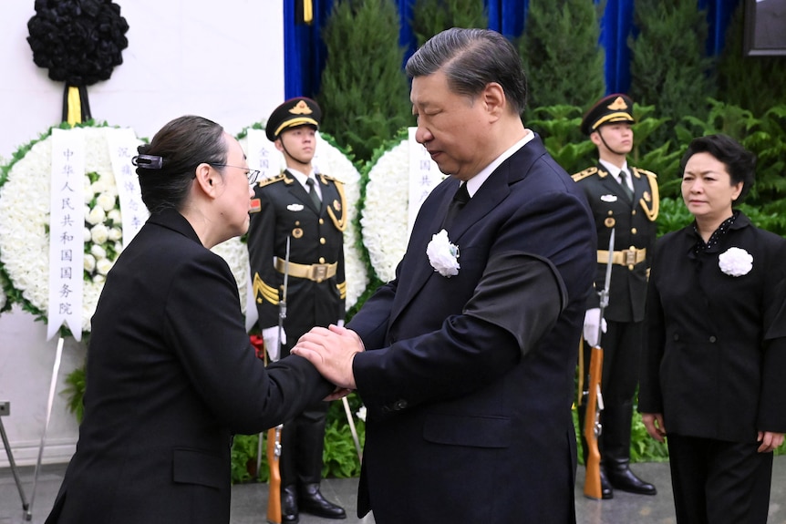 president xi, dressed in black with a white lapel flower, shakes hands with family member of li's