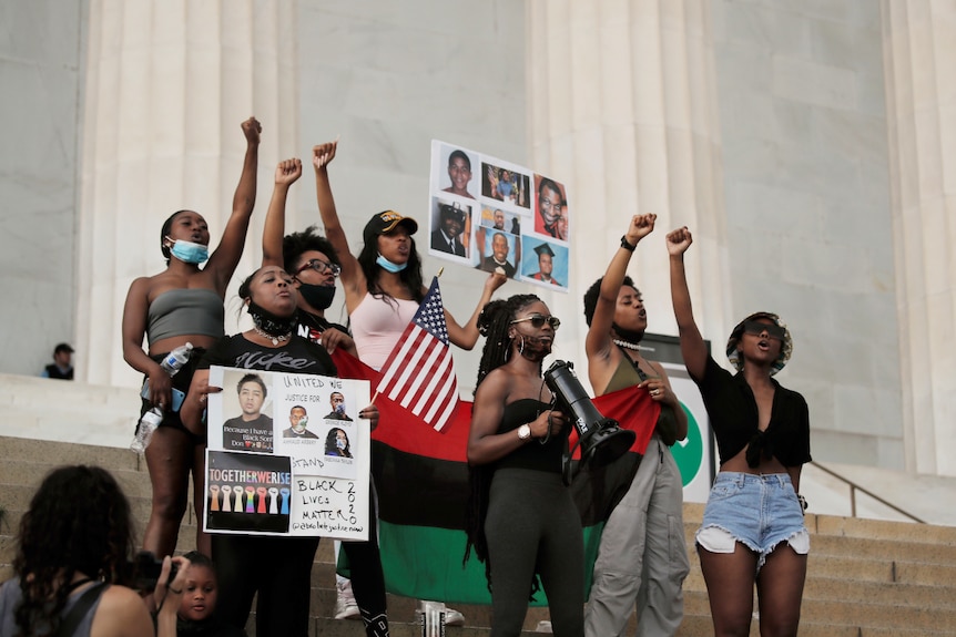 A group of young people stand on steps holding protest signs and holding their hands in the air