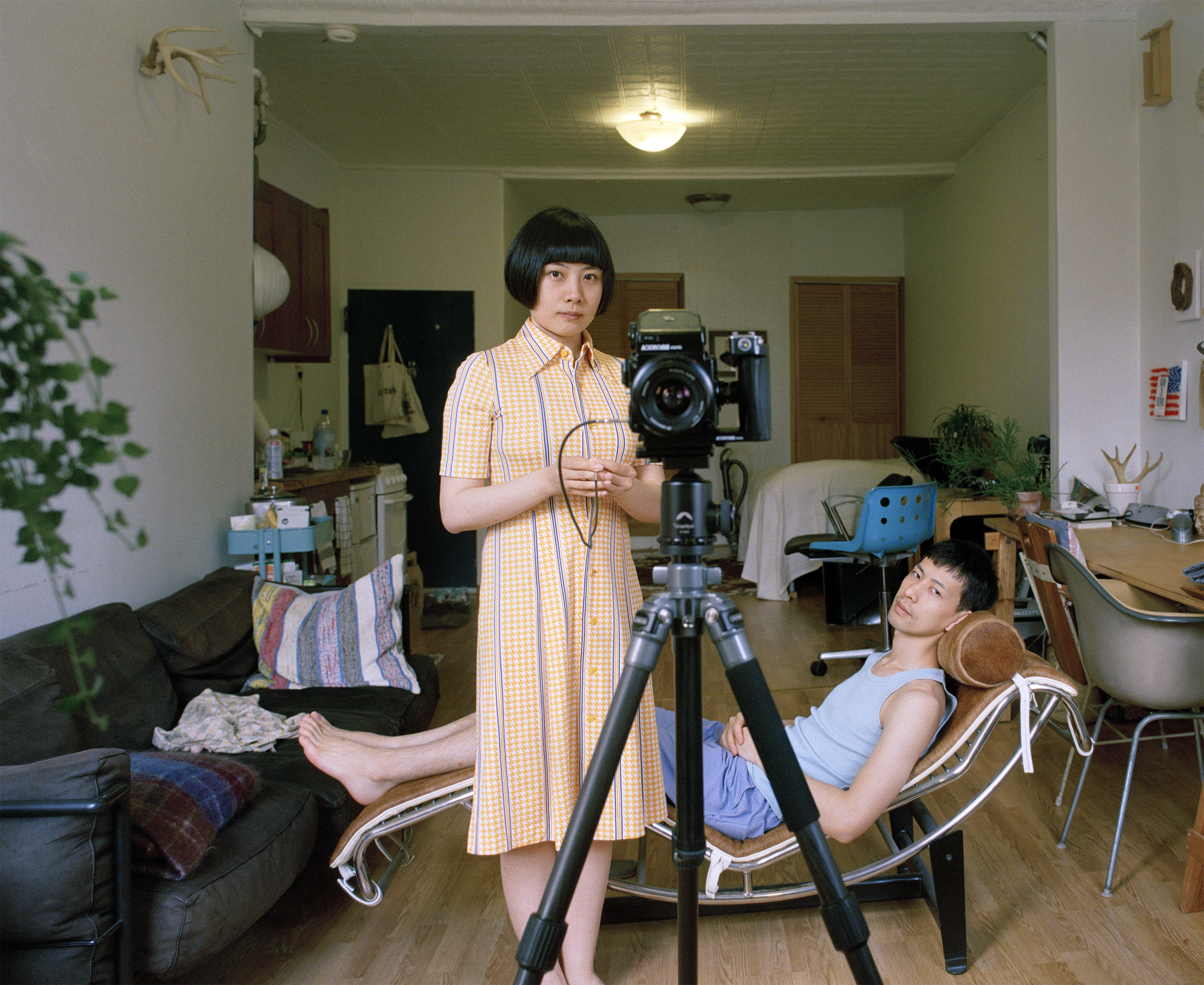 Pixy Liao, a Chinese woman with a dark bob wears a yellow dress and stands between a tripod and Moro, reclining in a chair
