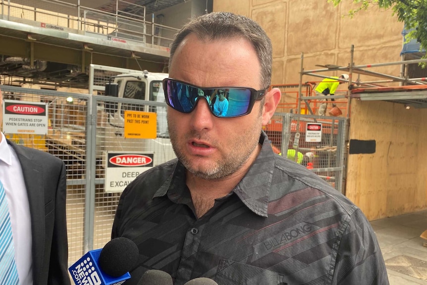 A man wearing sunglasses speaking to reporters outside court