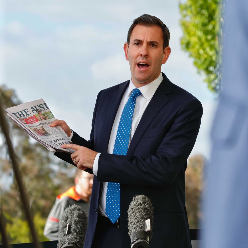 Labor MP Jim Chalmers speaks to reporters while holding a copy of the australian newspaper.