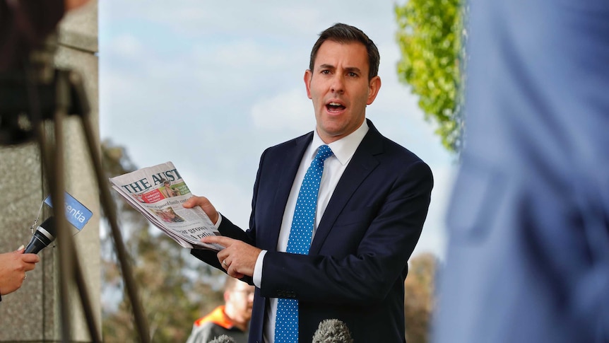 Labor MP Jim Chalmers speaks to reporters while holding a copy of the australian newspaper.
