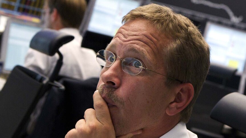A trader looks worried as he sits at his desk in front of the DAX board at the Frankfurt stock exchange
