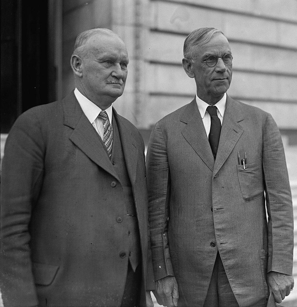 A black and white photo of two men wearing suits standing outside of Congress.