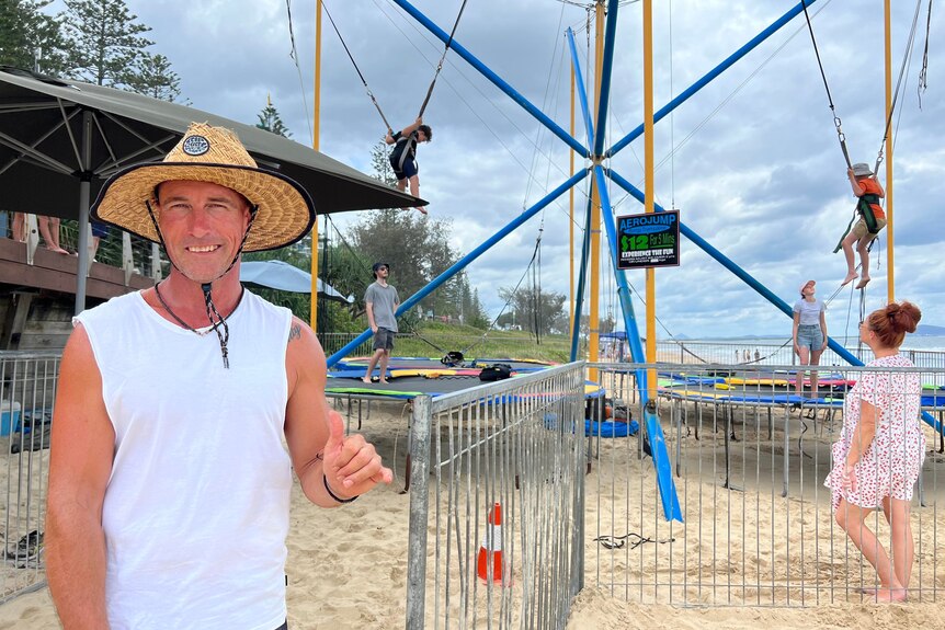 Man in straw hat standing in front of trampolines on the beach