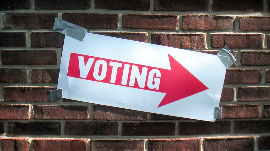 A sign with the word "voting" on a red arrow, taped to a brick wall.