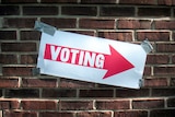 A sign with the word "voting" on a red arrow, taped to a brick wall.