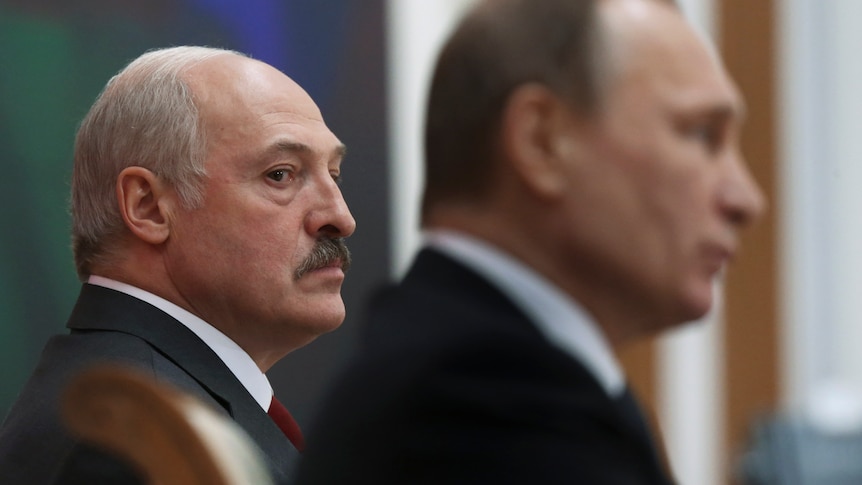 Alexander Lukasheko, a balding man with thick black moustache, glances towards out-of-focus Vladimir Putin in foreground