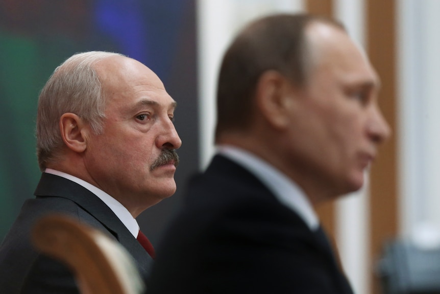 Alexander Lukasheko, a balding man with thick black moustache, glances towards out-of-focus Vladimir Putin in foreground