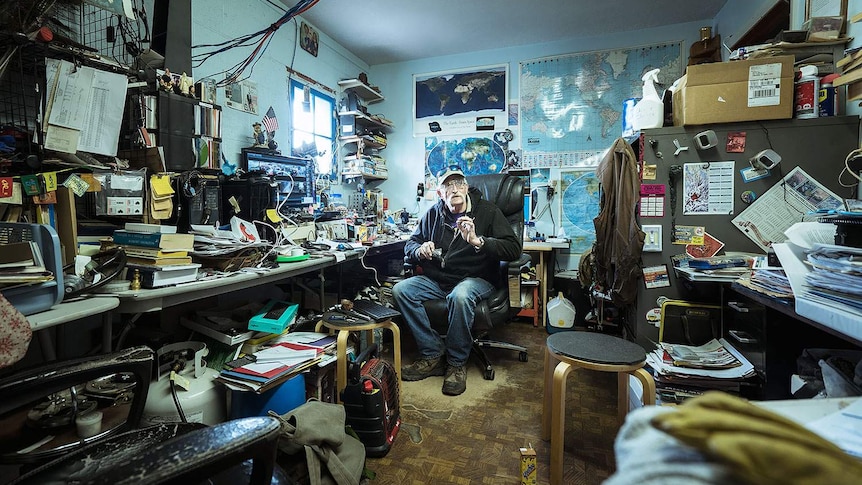 A man sits in an untidy office.