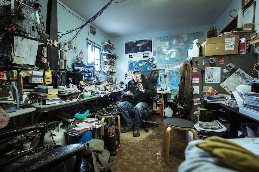 A man sits in an untidy office.