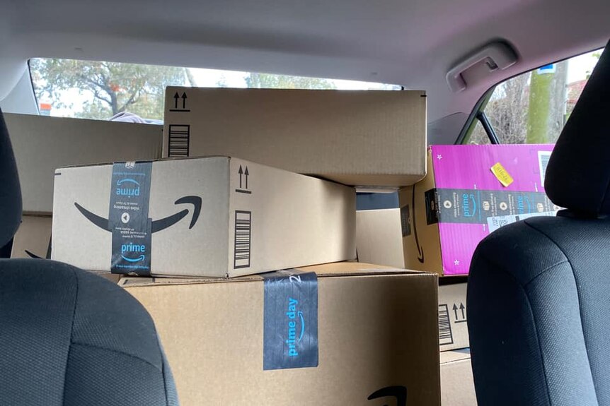 A stack of Amazon boxes in the back of a car obstructs the driver's view.