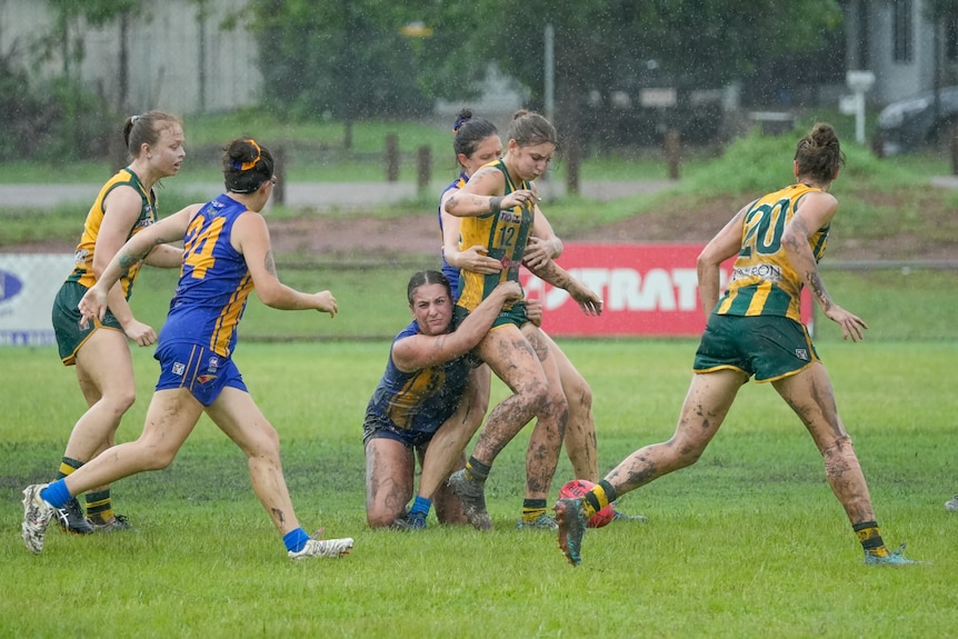 Players fight for the ball on the field in muddy and wet conditions.