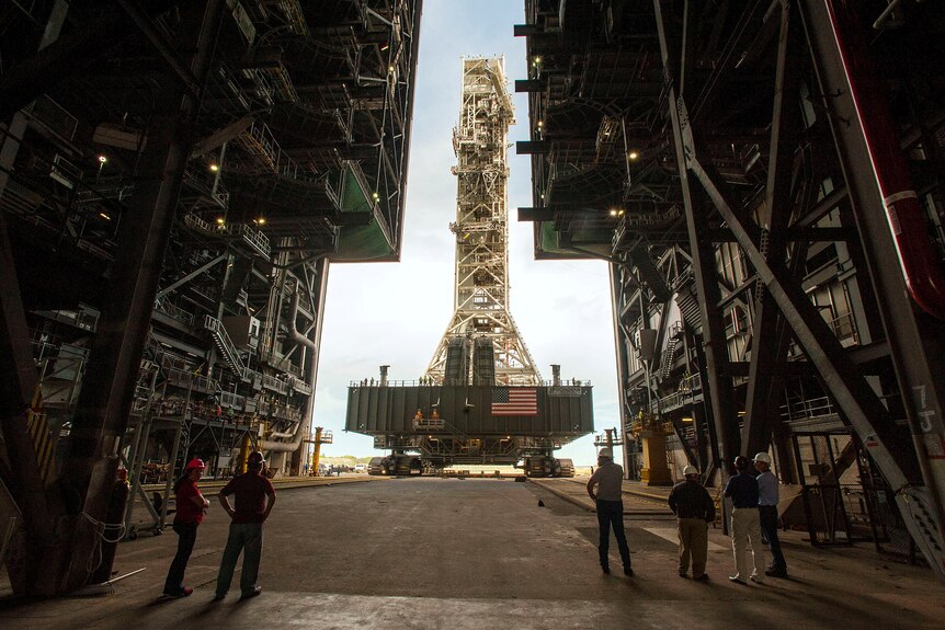 Workers wearing hard hats look on from inside the Vehicle Assembly Building as the Artemis launch tower is rolled back inside